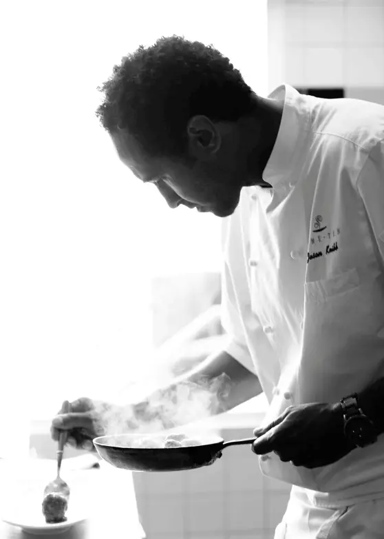 chef-right-image a black and white image of Chef Jason Knibb plating a dish. He is in sideview carefully placing food from a steaming skillet to a plate with a spoon