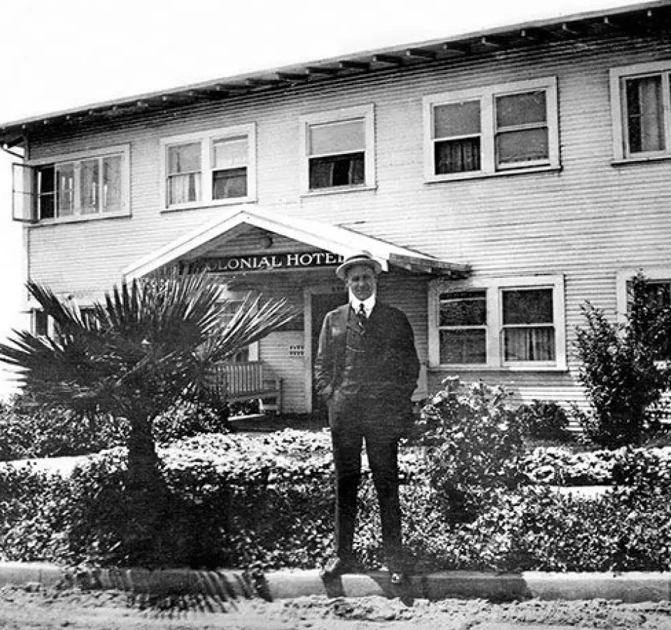 Old-photo-of-man-posing-in-front-of-the-hotel-1 An older photograph of a man standing in front of a building with a banner on the entry was reading 
