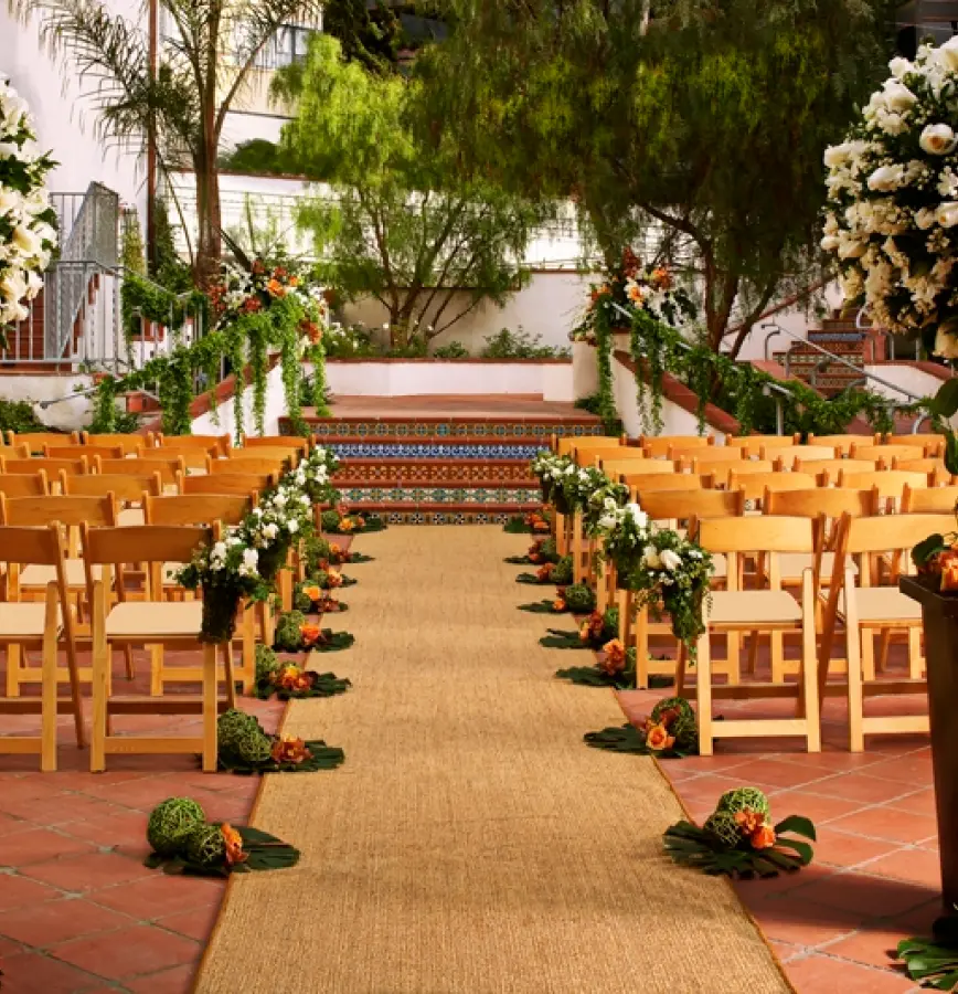 Rectangle-298 the courtyard arranged for a wedding with chair set up in rows with an isle down the middle leading to a short flight of stairs and landing