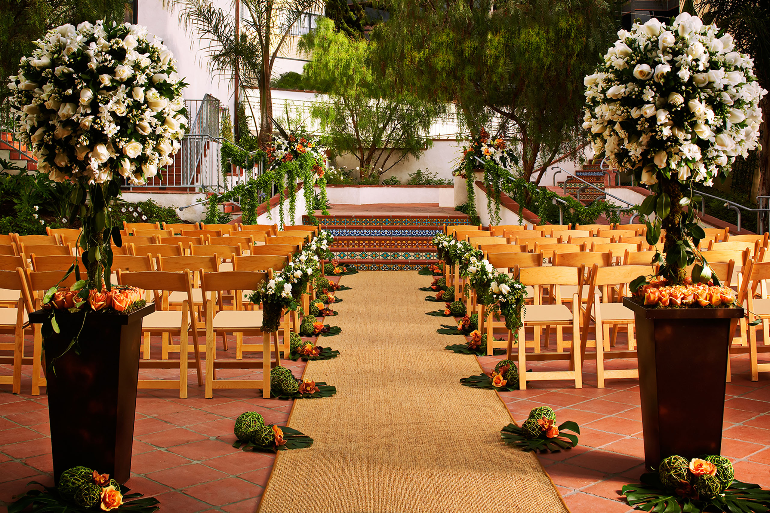 Grande-Colonial-Garden-Courtyard-Wedding A courtyard arranged with guest chairs facing a landing reached by a four step stair case. There are flower arrangements to either side of the path way