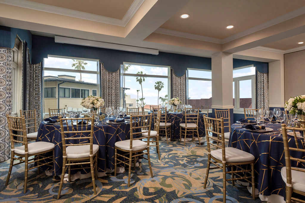 Grande-Colonial-Sun-Room-Social A restaurant seating area with three tables with place settings. The windows have a view of the surrounding buildings and palm trees