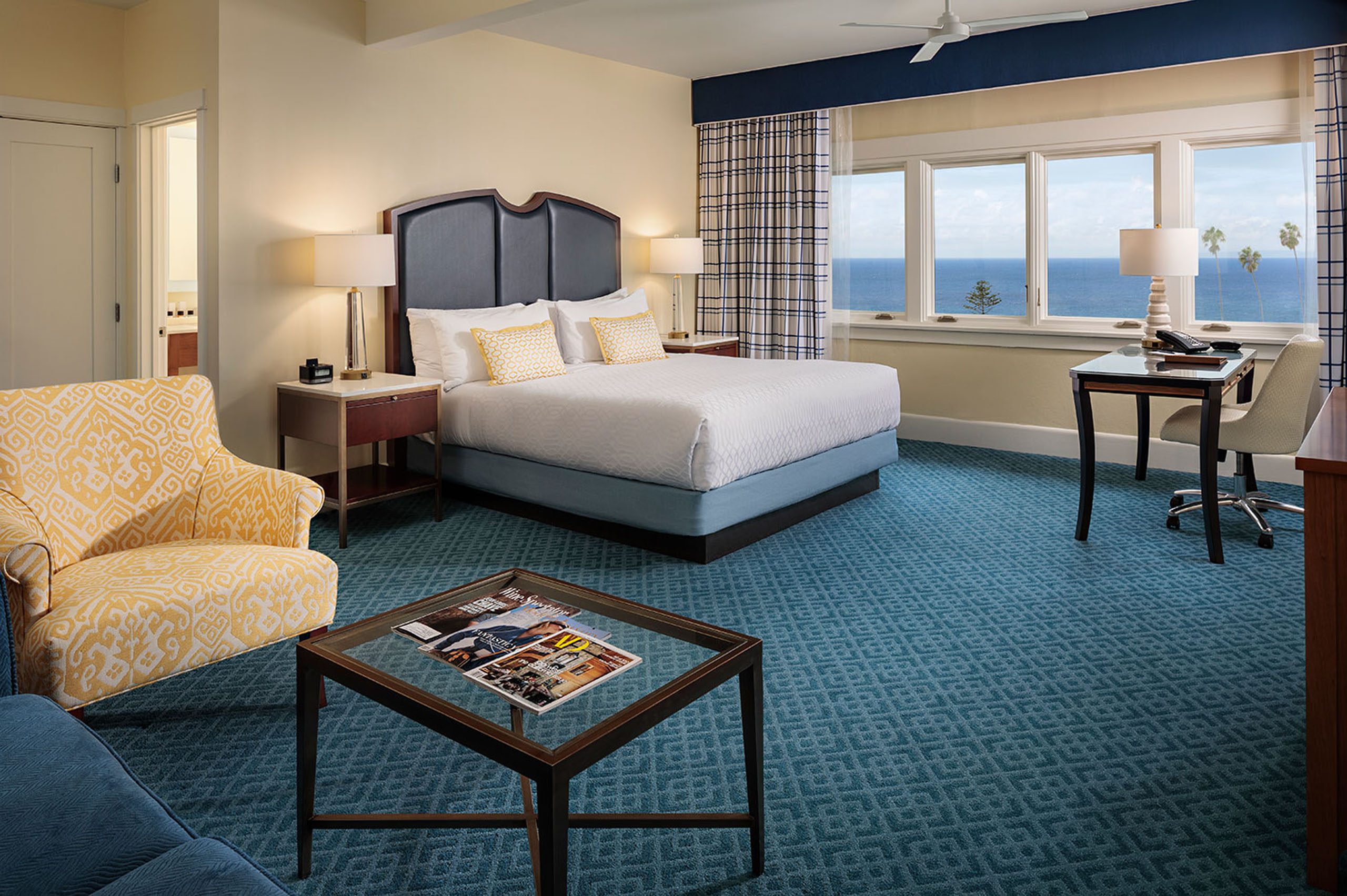grande-ocean-view-king-junior-suite - An ocean-view king sized hotel room with a bed, desk with chair, sitting chair, couch and coffee table.