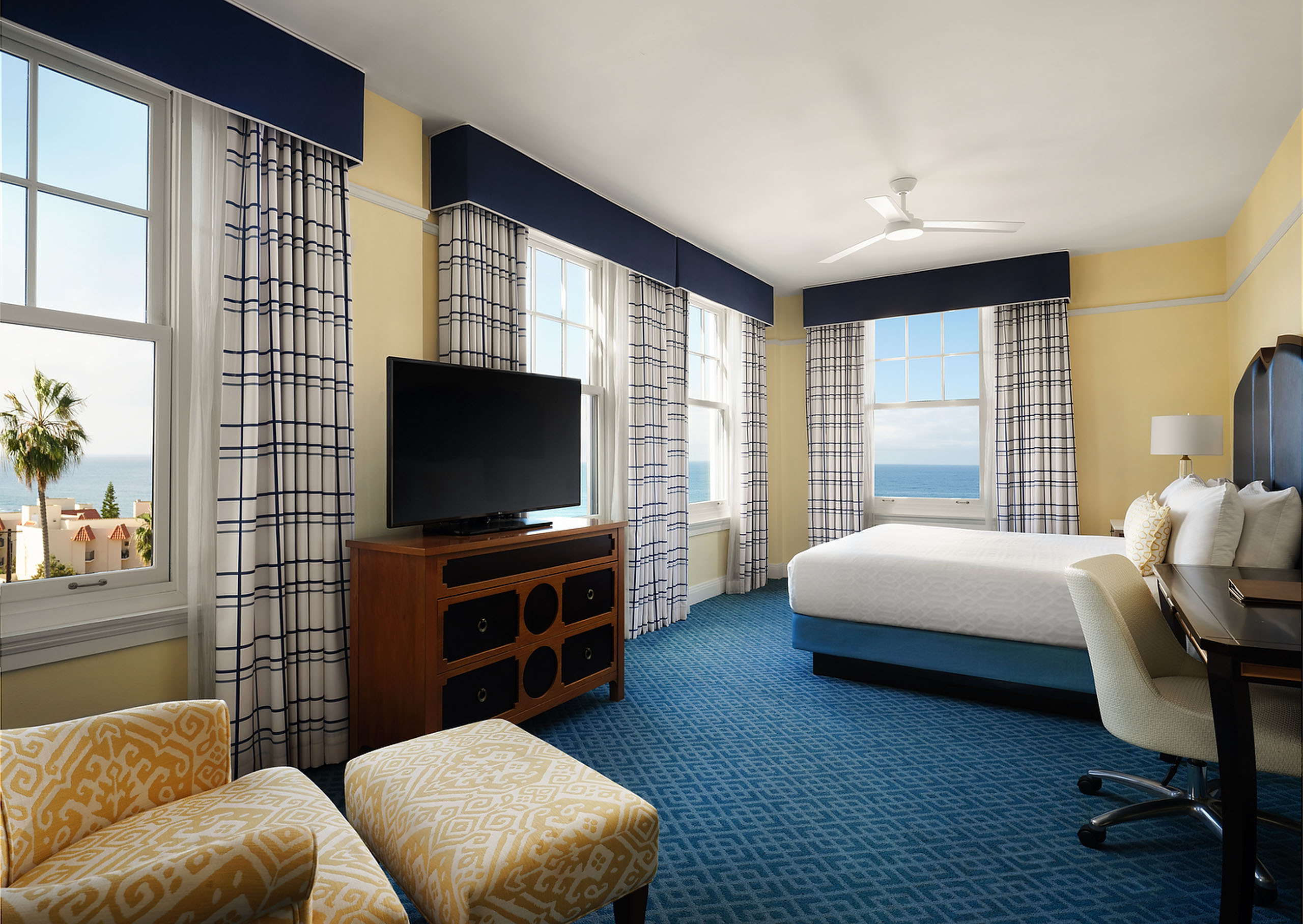 grande-colonial-ocean-view-grande-king - A ocean-view king sized hotel room showing a bed, desk with chair, sitting chair with an ottoman, and a TV on a dresser