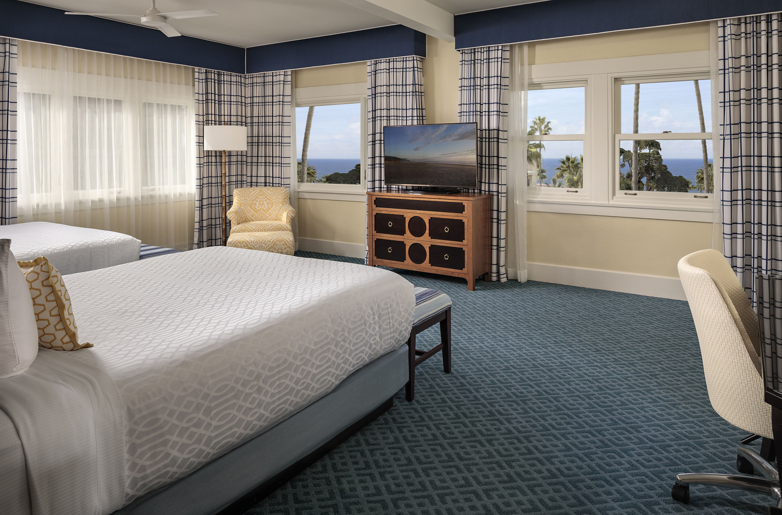 ocean-view-grande-queen-queen - An ocean-view hotel room with two queen-sized beds, a dresser with a tv and a sitting chair.