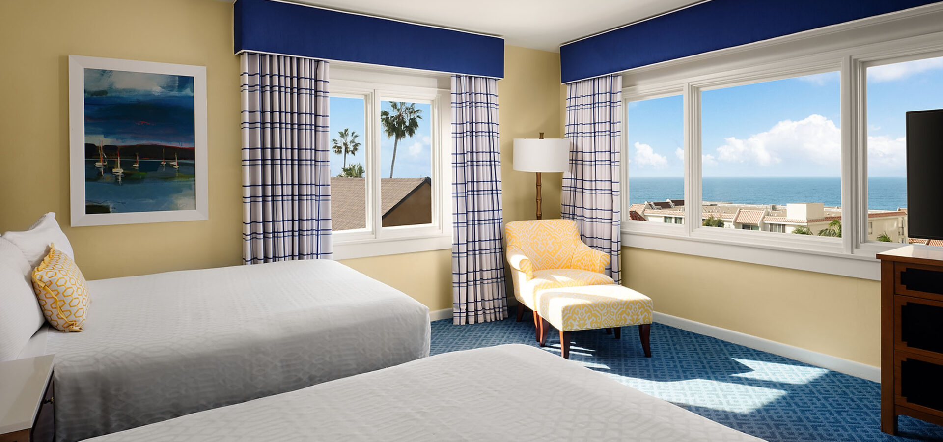 grande-colonial-ocean-view-suite-queen-queen - A double queen-sized bed suite with two windows and a sitting chair with ottoman