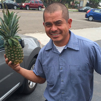 A man standing by a car holding a pineapple