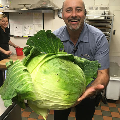 A man in a kitchen holding a very large cabbage