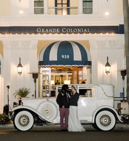 a bride and groom standing in front of the hotel with a white, vintage car