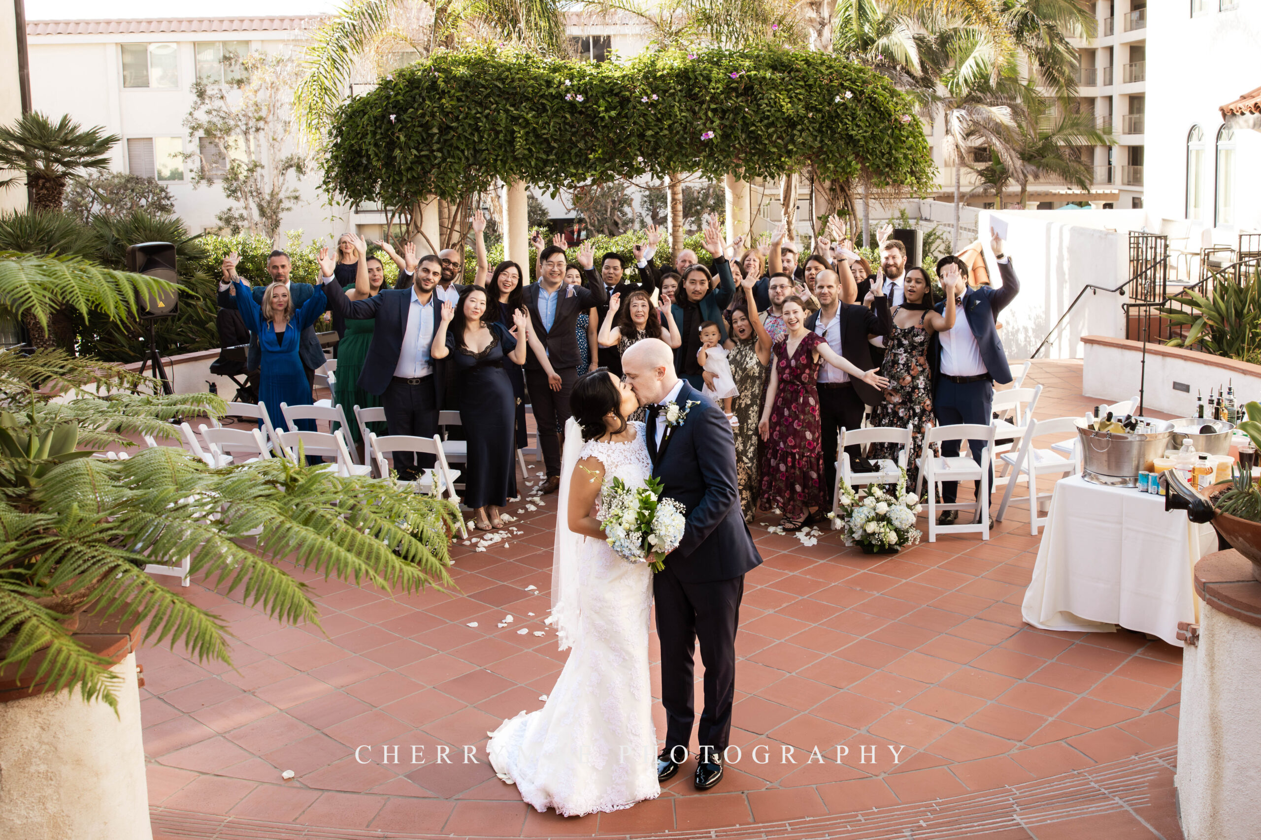 photo of bride and groom kissing with wedding party cheering in background